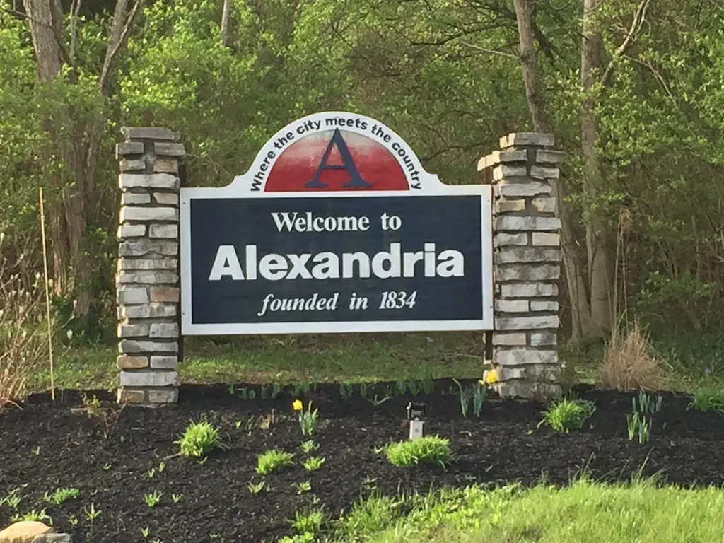 Alexandria KY | Davis Landscape Design & Installation Welcome sign for Alexandria with a dark blue panel reading 'Welcome to Alexandria' and 'founded in 1834' flanked by stone pillars in a green landscape.