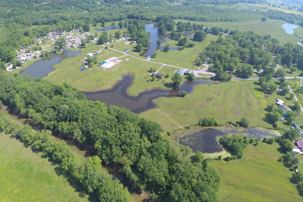 Big Bone | Davis Landscape Design & Installation Aerial view of a rural landscape with winding ponds, green fields, and dense trees surrounding a campground area and scattered houses.