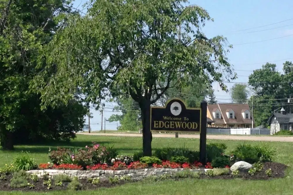 Edgewood-Kentuckypng | Davis Landscape Design & Installation Welcome sign for Edgewood in a landscaped flower bed with red flowers and a large tree, with houses in the background.