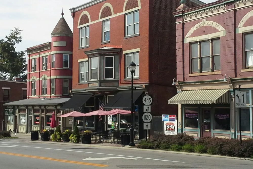 Fort-Thomas-Kentucky | Davis Landscape Design & Installation Quaint downtown street with red brick storefronts, outdoor seating under pink umbrellas, and planters along the curb.