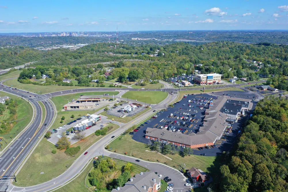 Taylor-Mill-Kentuckyjpg | Davis Landscape Design & Installation Aerial view of a suburban shopping plaza with a large parking lot, bordered by roads and dense green trees.