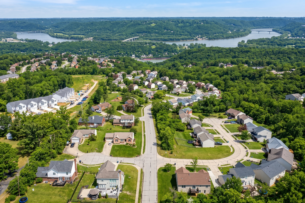 Francisville Kentucky | Davis Landscape Design & Installation Aerial view of a suburban neighborhood with tree-lined streets, houses, and a river with bridges in the distance.